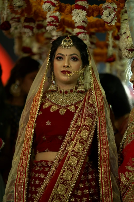 a woman dressed in red and gold is standing under a canopy of flowers