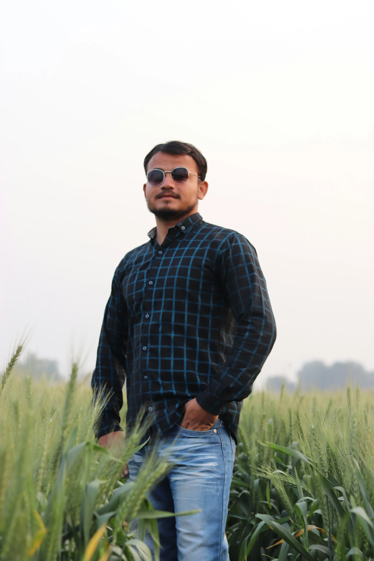 a man in blue jeans and sunglasses is standing in a field