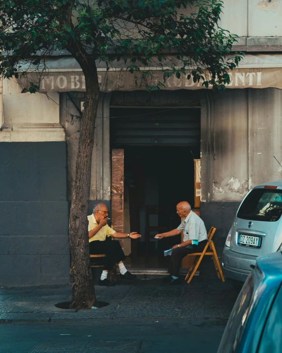 two men in chairs sitting on a sidewalk holding hands