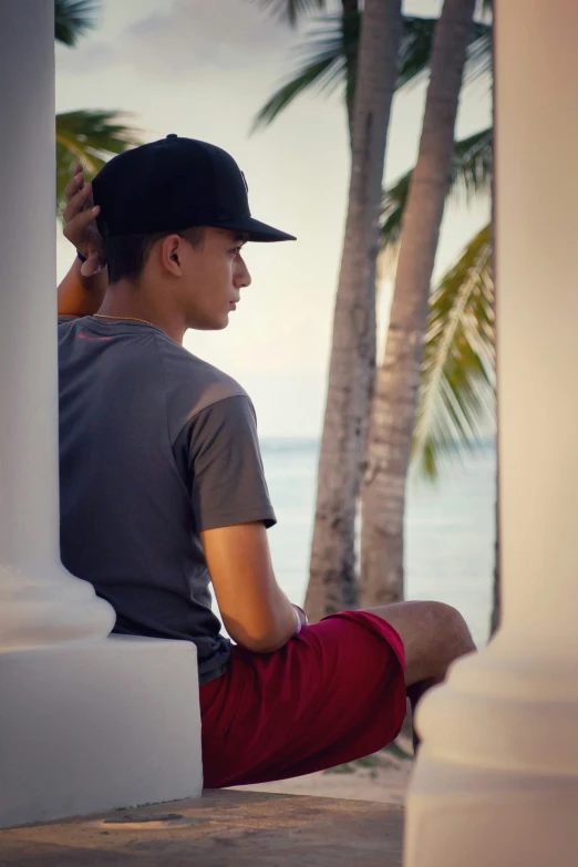 a young man sitting on the wall looking over at the ocean