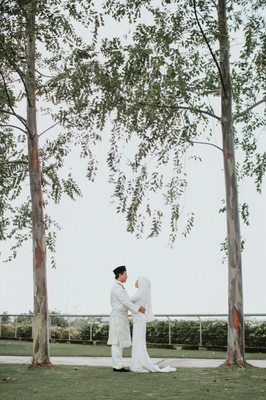 the man is wearing white near two tall trees