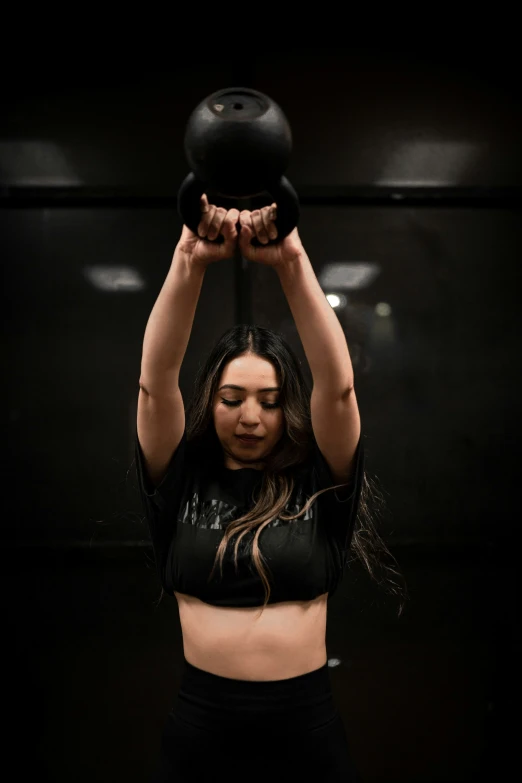 a beautiful woman holding a black dumbbell over her head