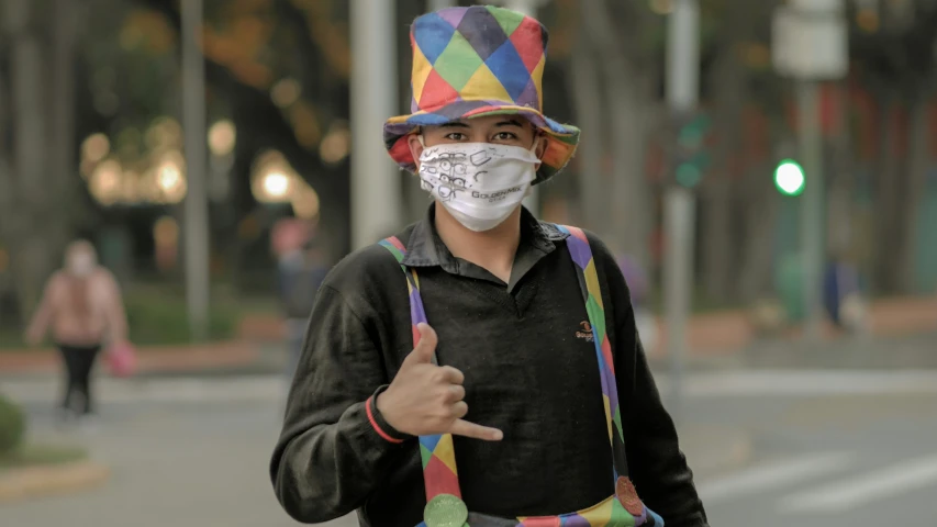 a man standing in the street wearing a mask, giving a peace sign