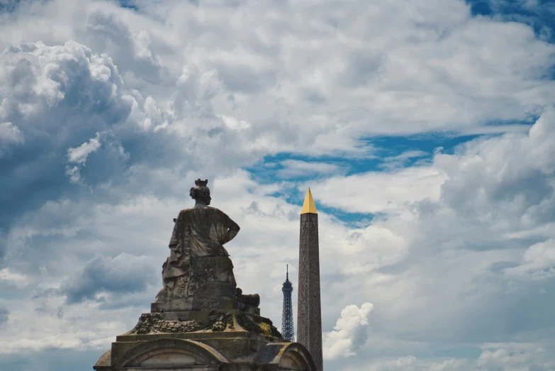 a very tall statue next to a pillar in the sky