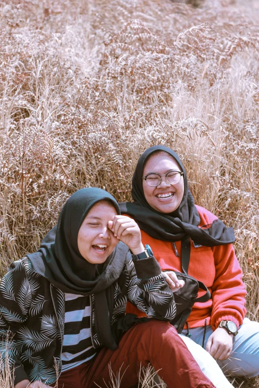 two women pose for the camera while sitting on a field