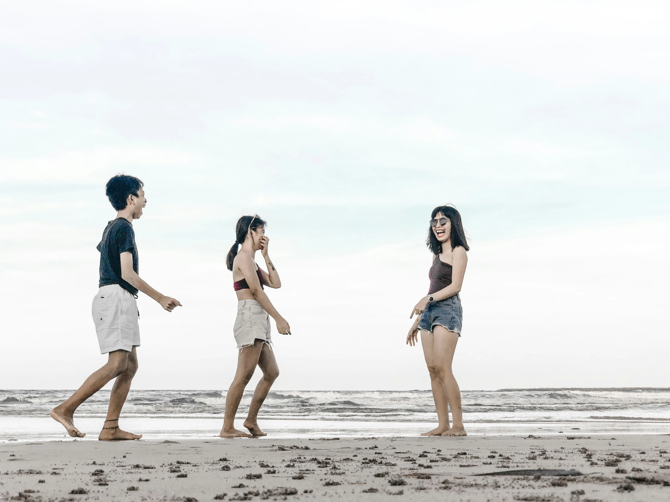 three young people standing on the beach by a body of water