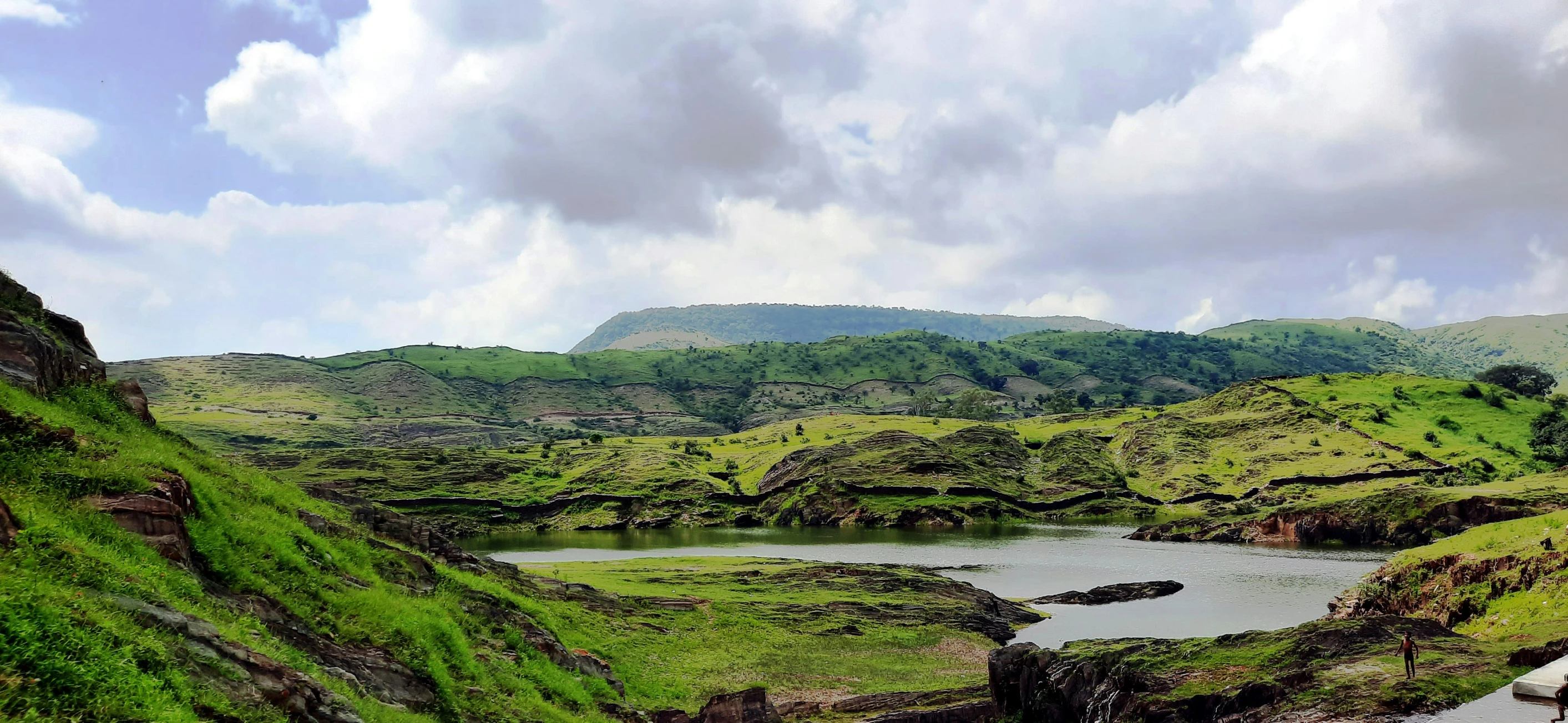 a lush green mountain with small pond surrounded by trees