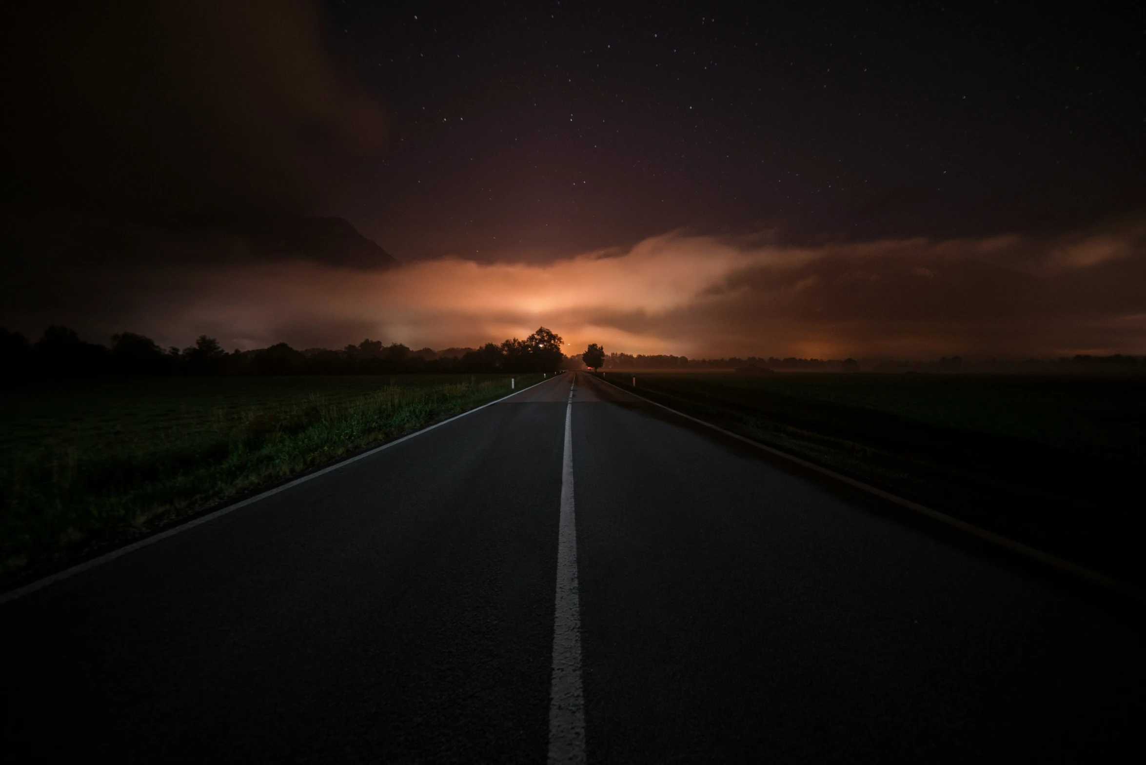 a dark and ominous sky is shown as the sun sets over an empty road