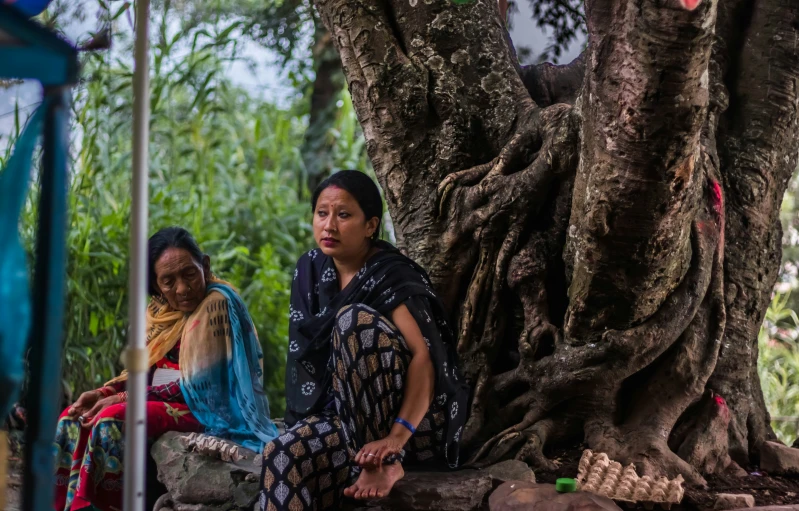 two women are sitting on the ground near a tree