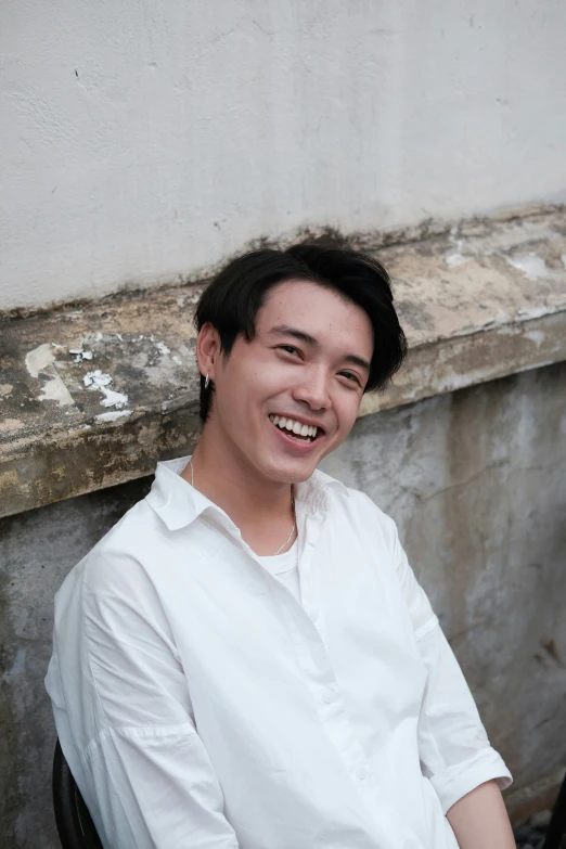 an asian man smiles while seated outside