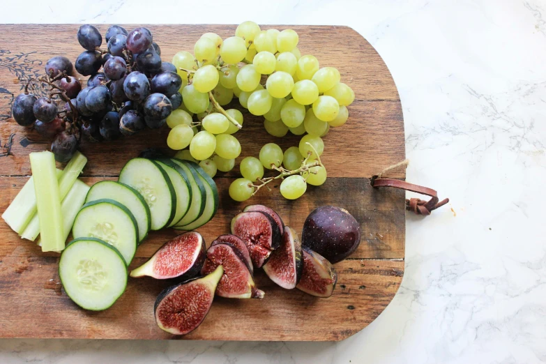 sliced cucumber, sliced olives, slices of fig tree and other fruit on a wooden  board