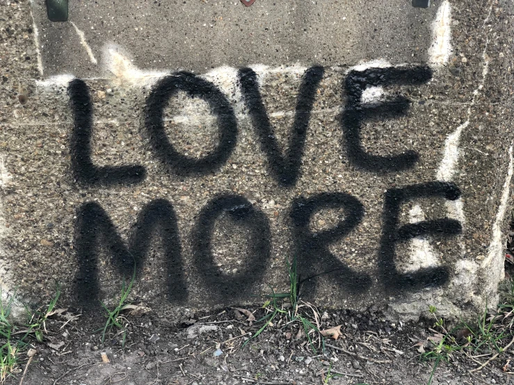 graffiti writing that says love more on the sidewalk