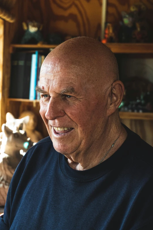 a bald man smiles while standing near a wooden shelf