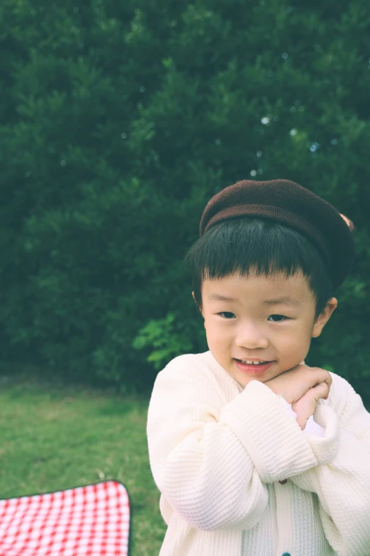 a small boy with his hands on his chest and a checkered table cloth behind him