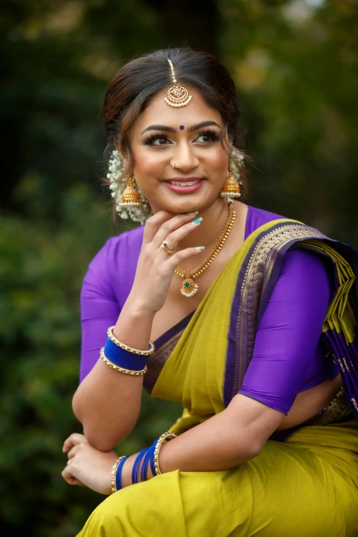 a beautiful woman sitting on a chair wearing a sari and gold jewelry