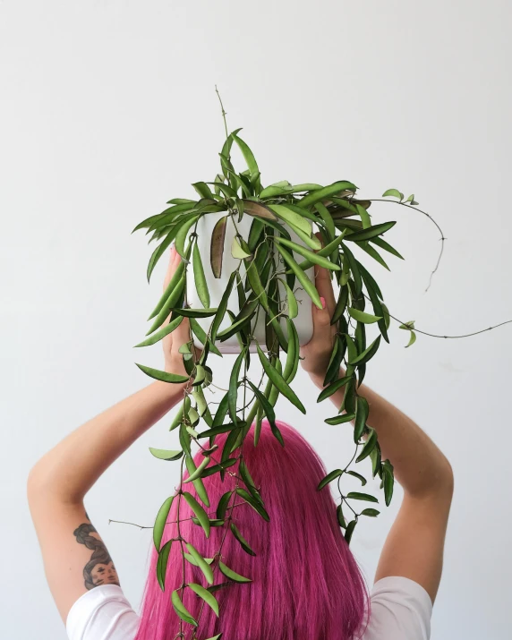 a woman wearing a white shirt carrying green leaves across her head