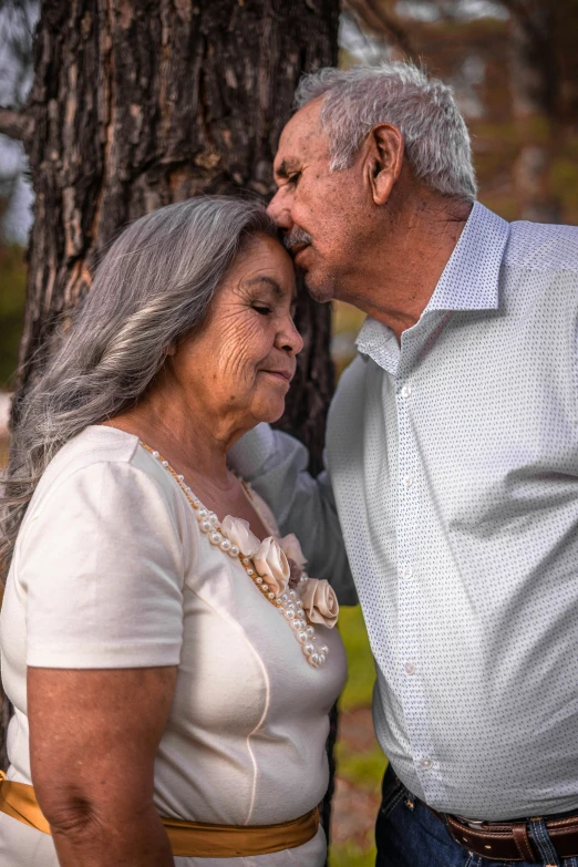 a man and woman leaning against a tree, one is holding the other's neck