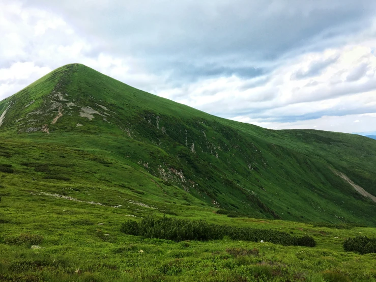 a green grass covered mountain near a cloud filled sky