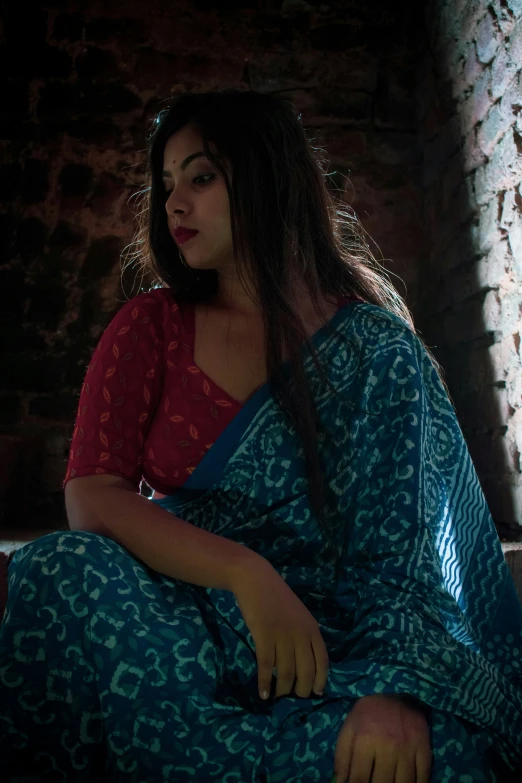 a woman wearing a blue and red sari sits in the middle of a room