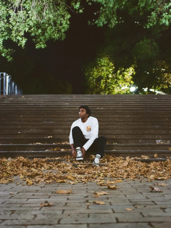 a man in white shirt sitting on steps with his feet in leaves