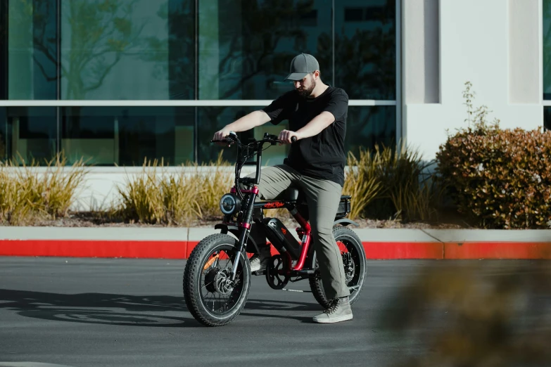 a man with grey cap and gray jeans rides a red, black and black bike