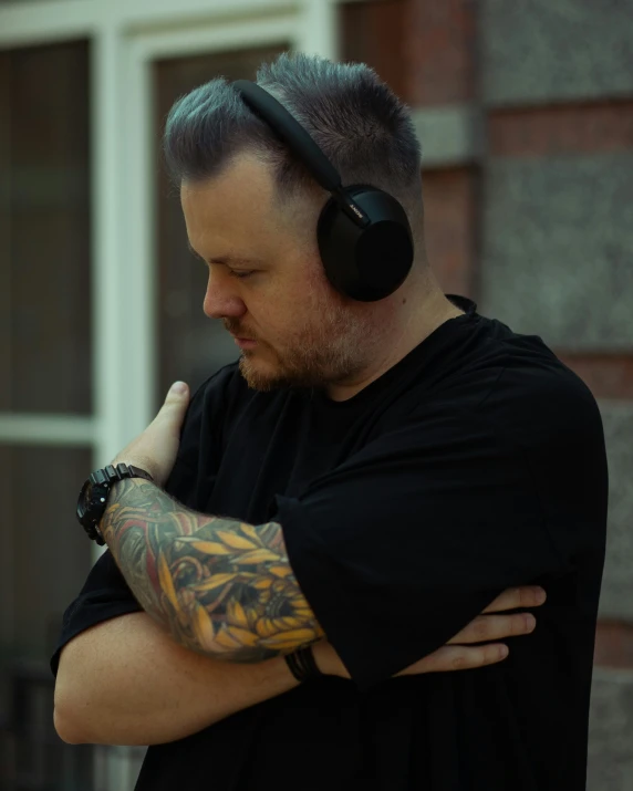 a man with a tattooed arm and headphones is looking down at his ear