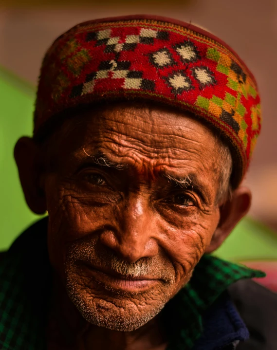 an old man with a hat on his head looking at the camera