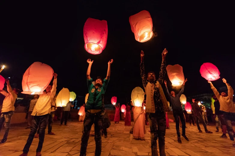 people standing and holding lanterns in the air at night