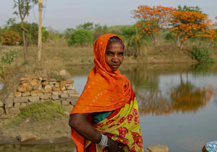 a woman in an orange shawl stands next to a lake