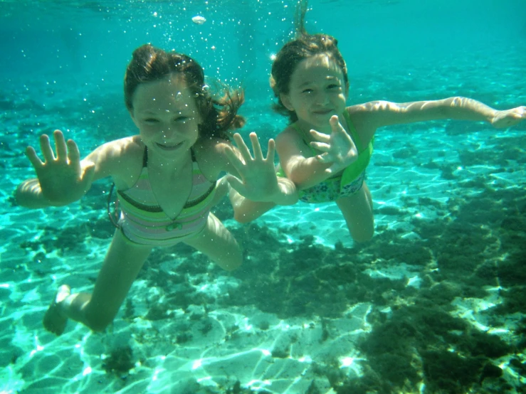 two girls underwater, holding their hands up to the camera