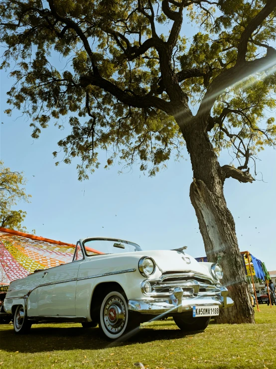 an old convertible car parked under a tree in the grass