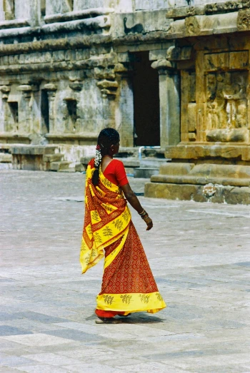 a woman in red, yellow and gold in front of ruins