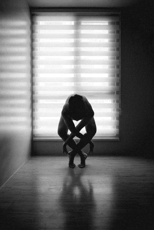 a man kneeling on a hard wood floor in front of a window with blinds