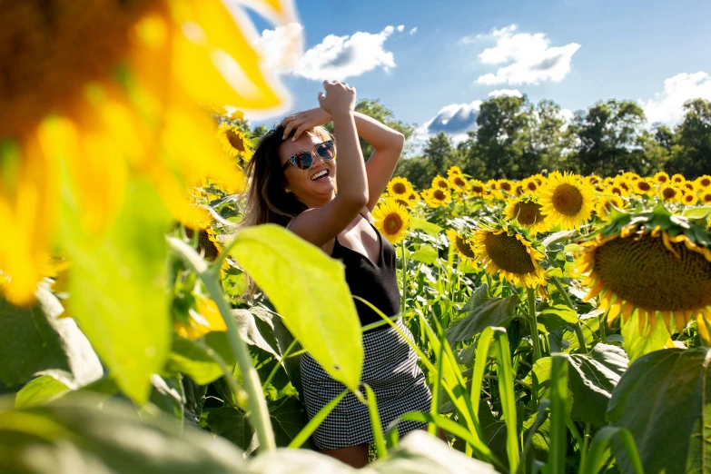 a beautiful woman wearing sunglasses stands amongst yellow flowers in the field