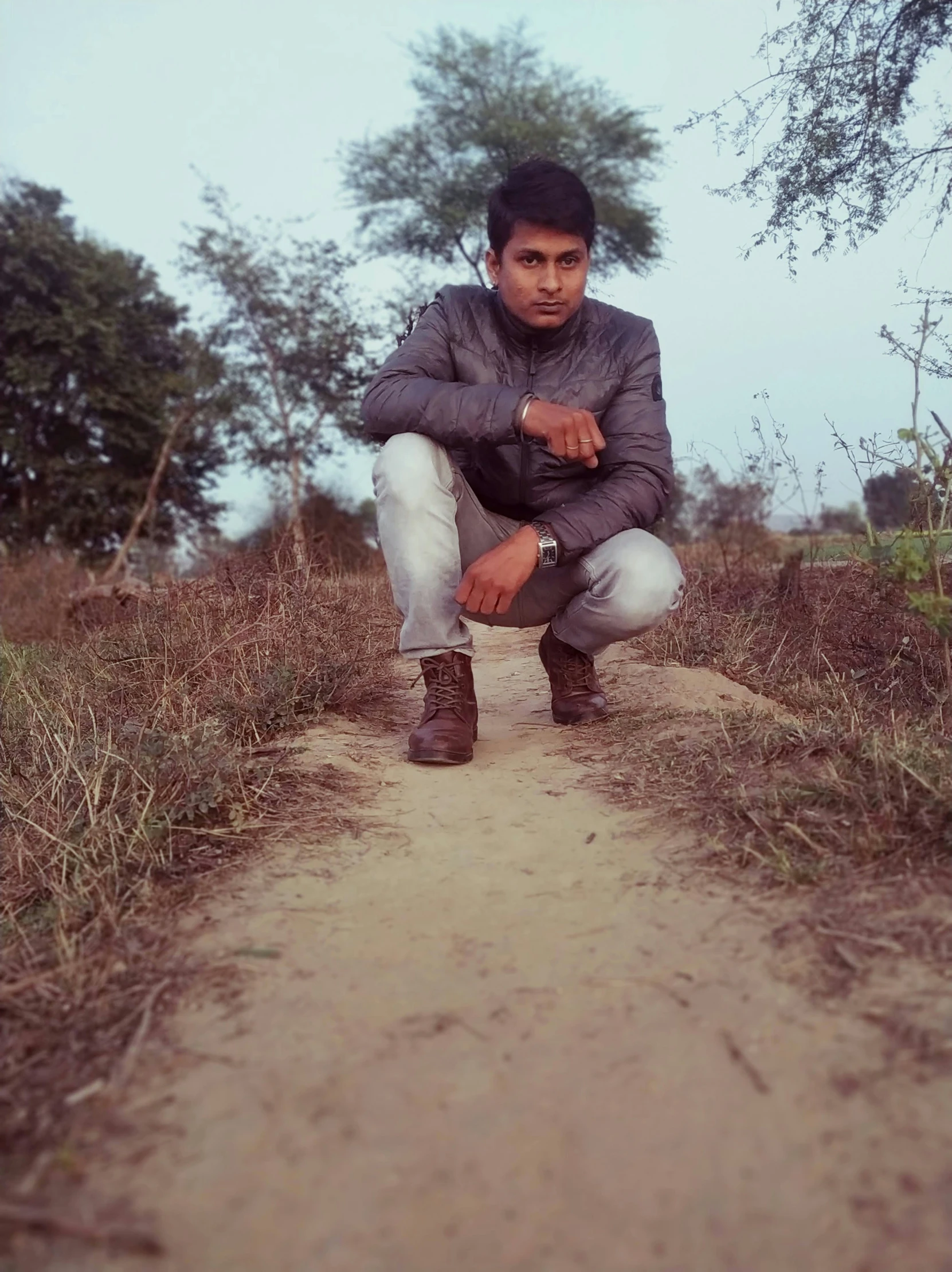 a young man kneeling on a trail near some trees