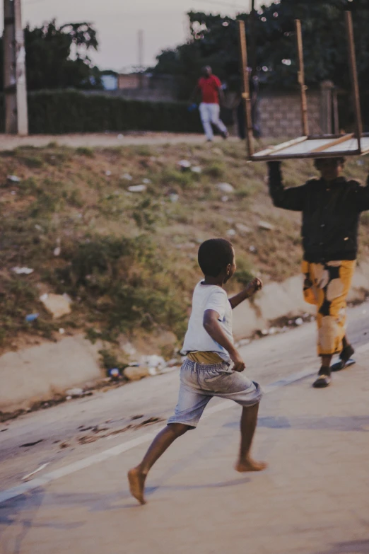 two children playing soccer on the road with others walking nearby