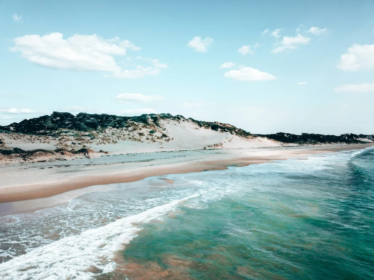 a beach in front of a white dune near the ocean