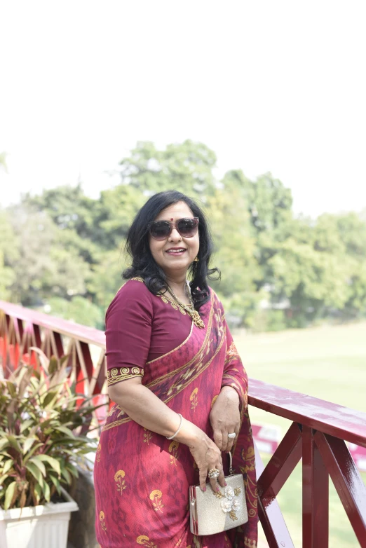 a woman is standing on a bridge wearing a maroon sari
