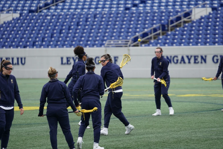 five female lacrosse players in blue uniforms stand on the field