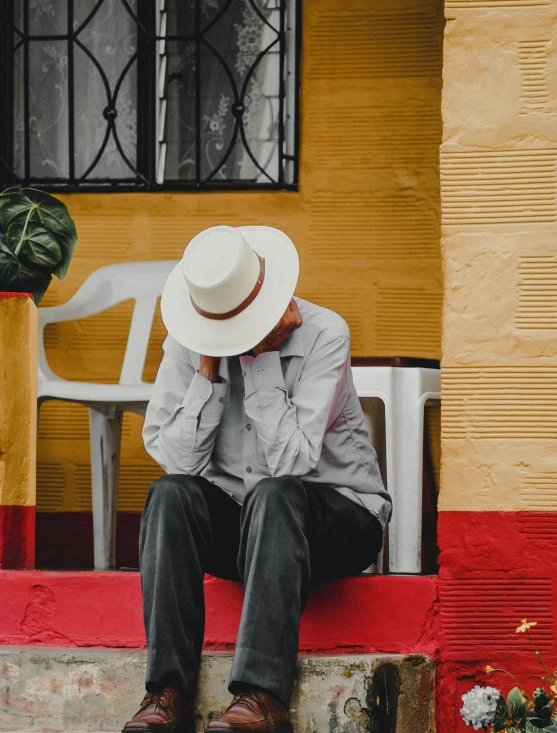 man in hat and slacks sitting on steps with hand near face