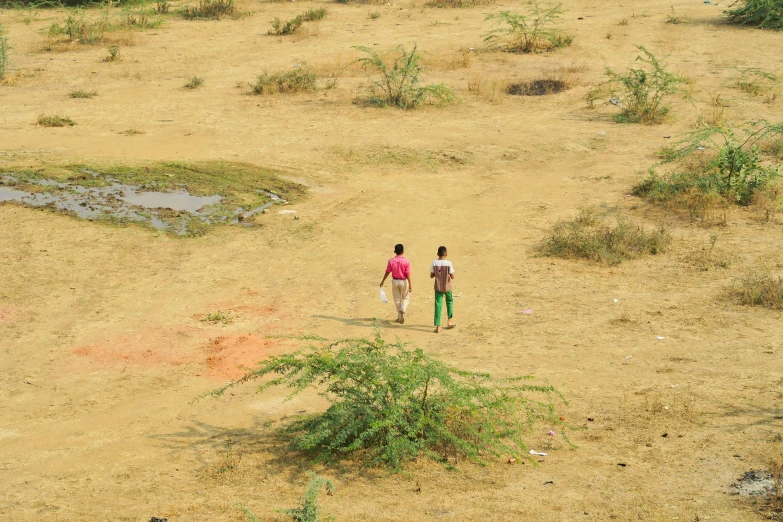 two people walking in the dirt area next to a tree
