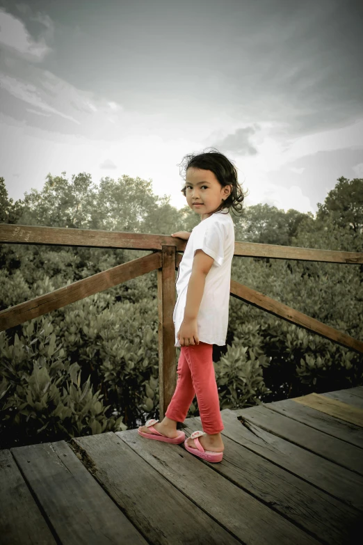 a girl on a wooden bridge smiles as she stands with her hand on her hips