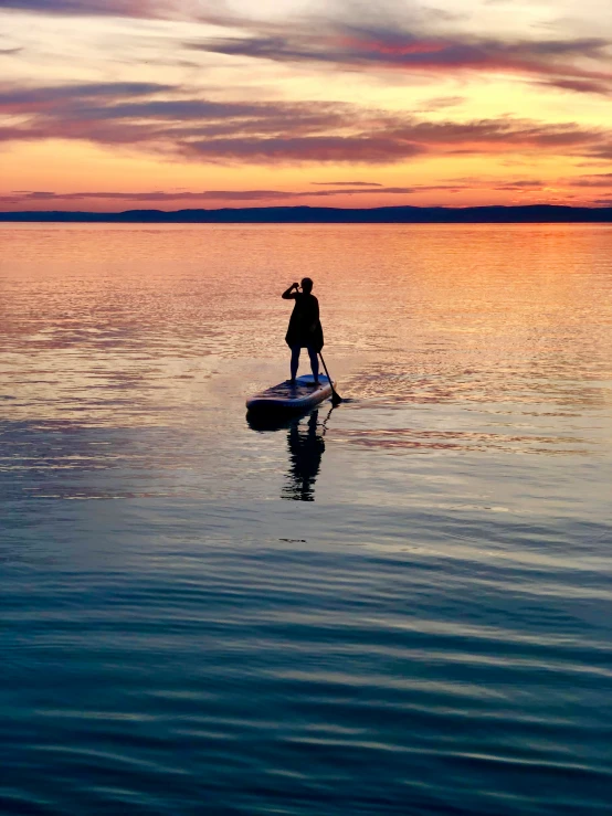 a person standing on the edge of a boat in the water at sunset