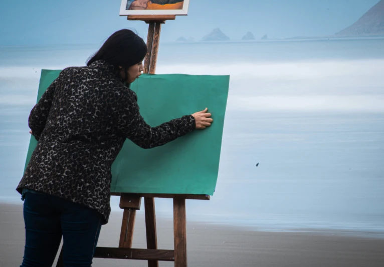 a woman writing on a piece of paper while standing next to a easel