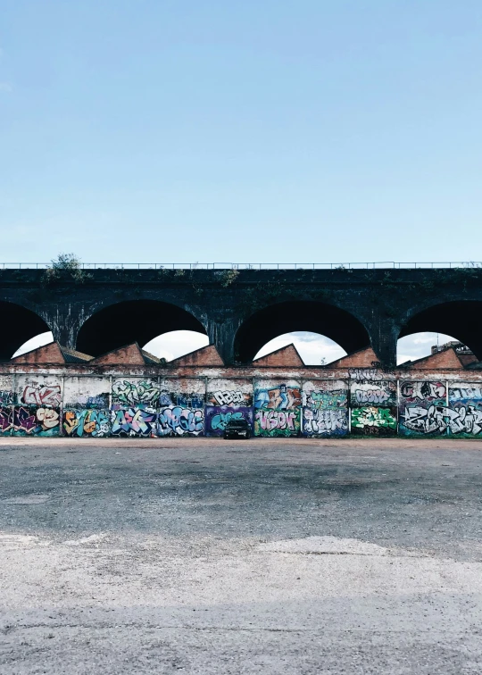 a person is standing in the middle of an empty parking lot next to a concrete wall with graffiti