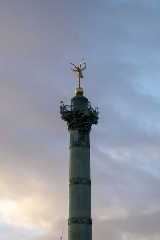 a tall statue with an angel on top that stands in front of some buildings