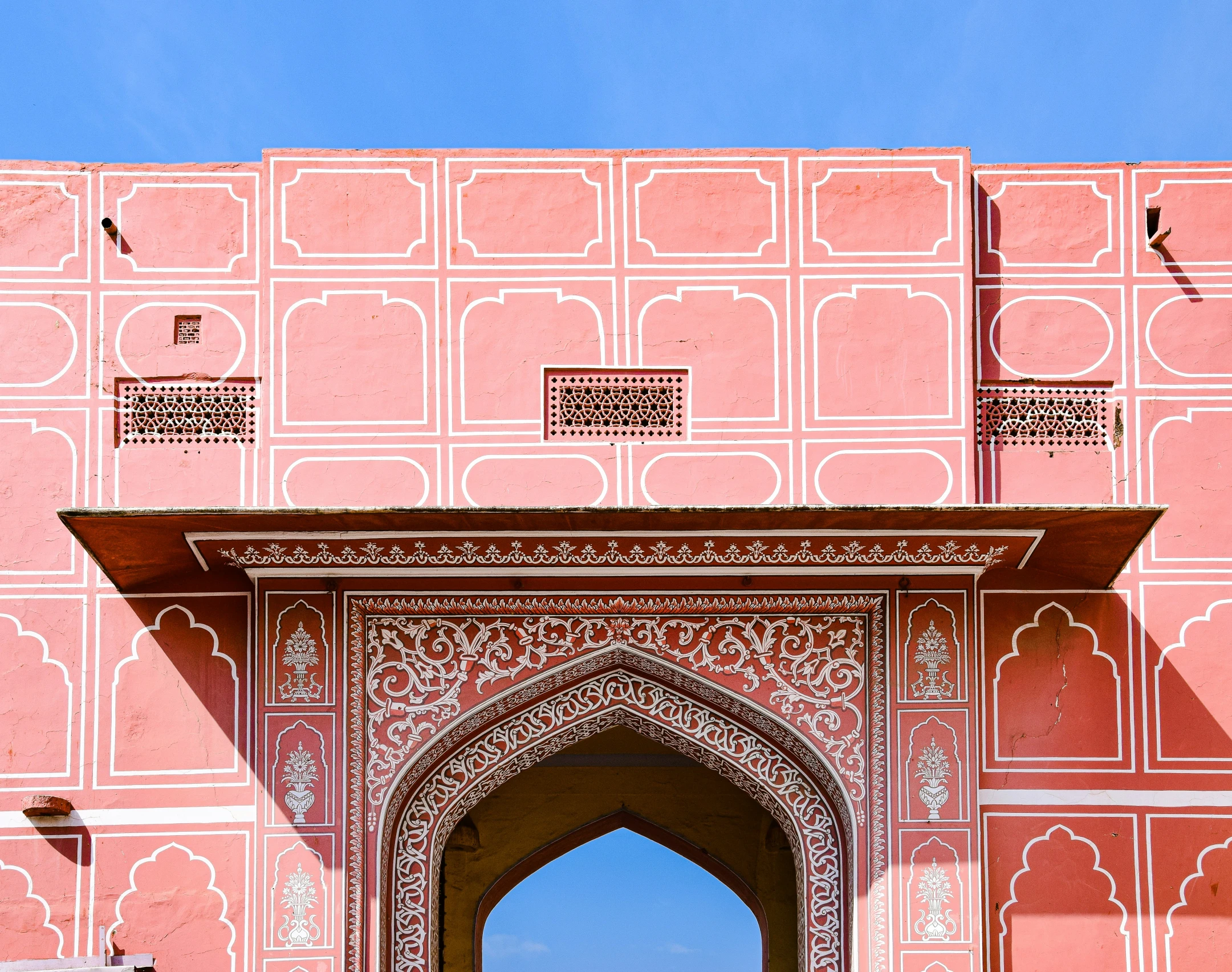 an ornate archway leading to the sky in front of pink and white walls