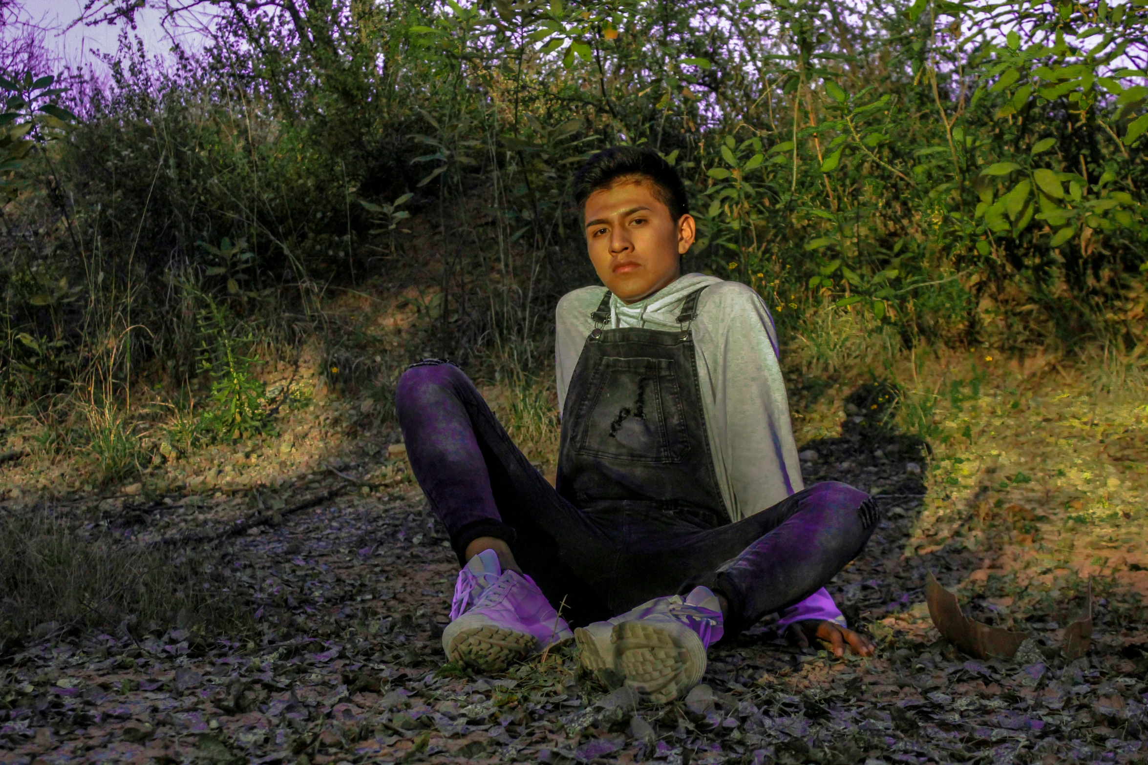 a person sitting on some dirt in front of bushes