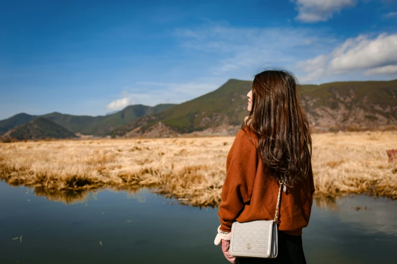 a woman in an orange sweater and black pants looks out over the water