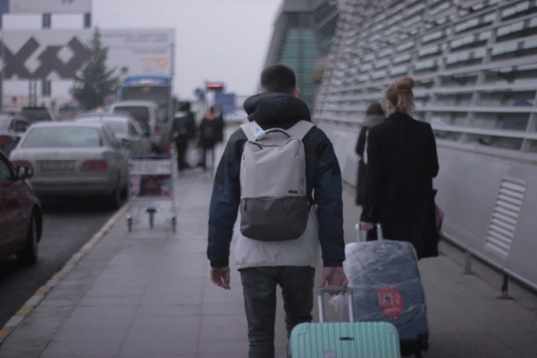 a man with a backpack pulling suitcase and cart next to cars